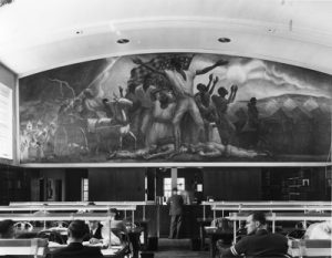 Black and white photo of the Curry mural with the library's circulation desk underneath.