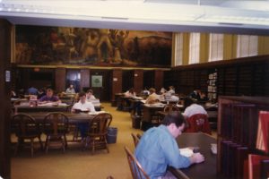 A color photo of students studying underneath the mural, taken from closer to the entrance of the room.